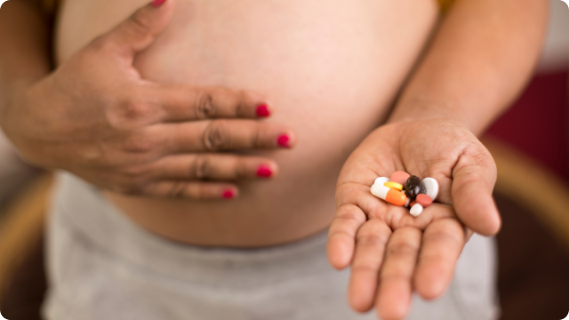 A pregnant woman holding out vitmains and pills.